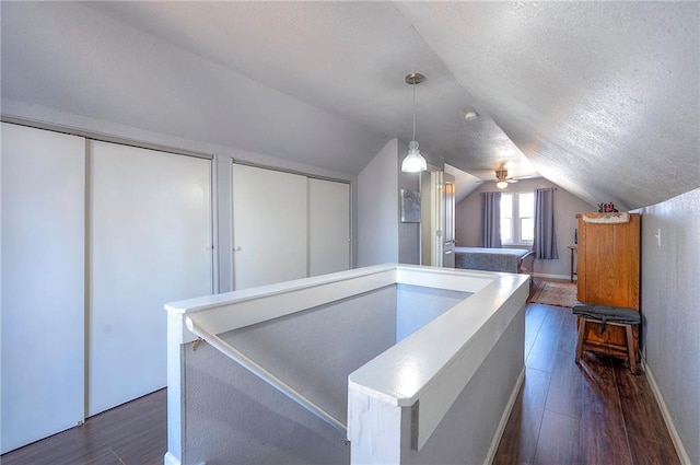 hallway featuring baseboards, a textured ceiling, dark wood-type flooring, and lofted ceiling