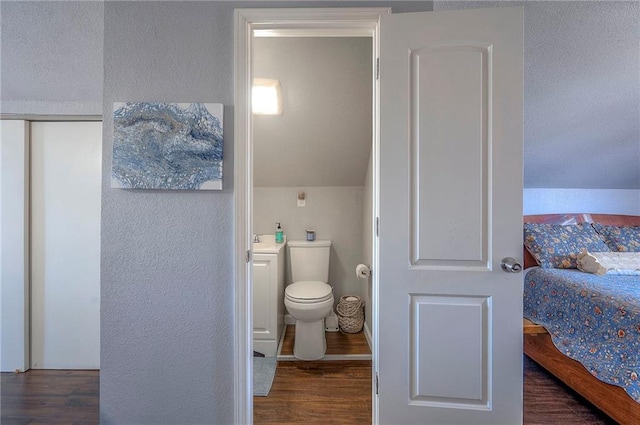 bathroom with toilet, wood finished floors, and a textured wall