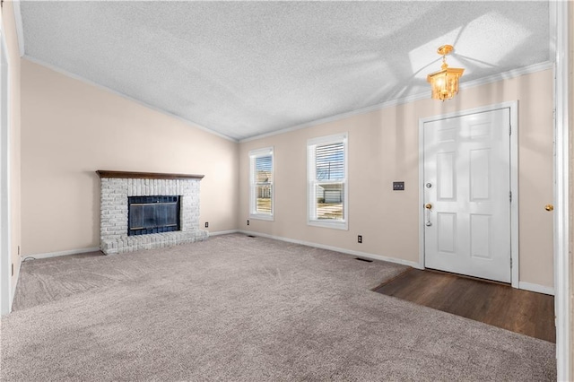 unfurnished living room with a textured ceiling, carpet flooring, crown molding, lofted ceiling, and a brick fireplace