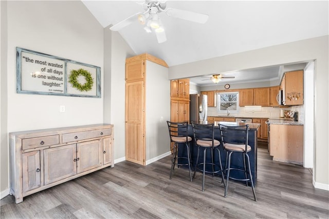 kitchen featuring dark wood-style floors, appliances with stainless steel finishes, a breakfast bar area, baseboards, and vaulted ceiling