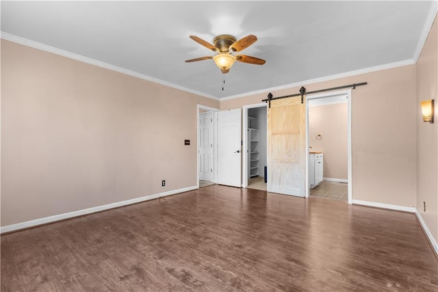 unfurnished bedroom with a barn door, baseboards, wood finished floors, and crown molding