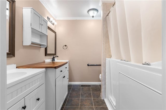 full bath with baseboards, two vanities, a sink, crown molding, and toilet