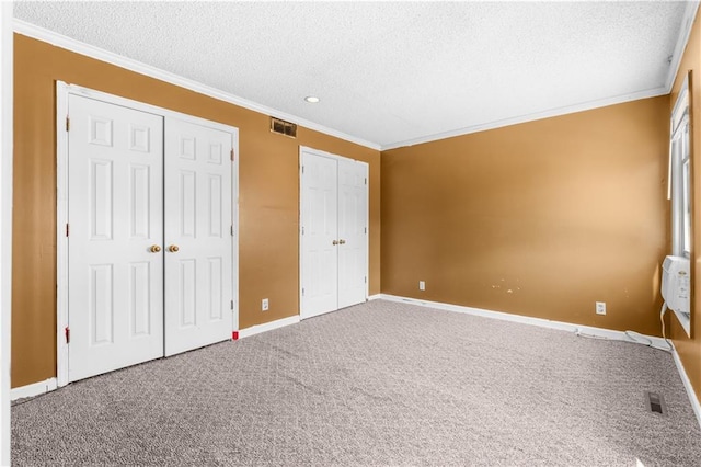 unfurnished bedroom featuring visible vents, a textured ceiling, multiple closets, and ornamental molding