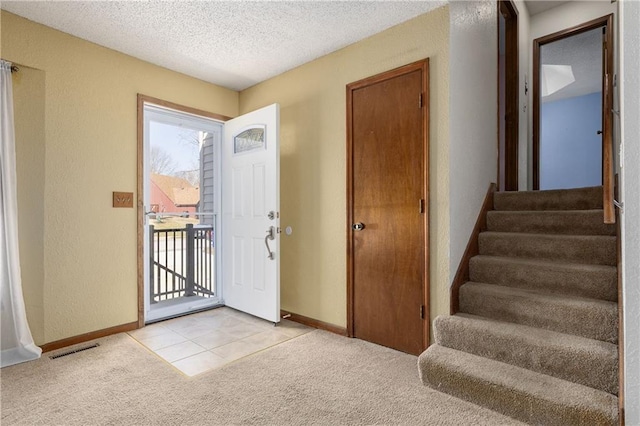 foyer entrance with a healthy amount of sunlight, visible vents, stairs, a textured ceiling, and light colored carpet