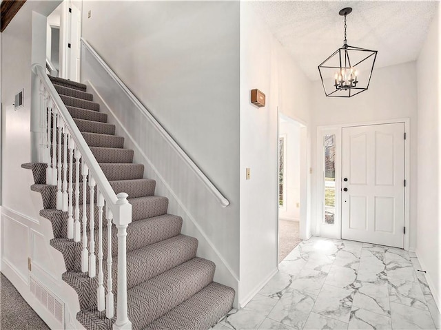 entryway with baseboards, visible vents, stairs, marble finish floor, and a chandelier