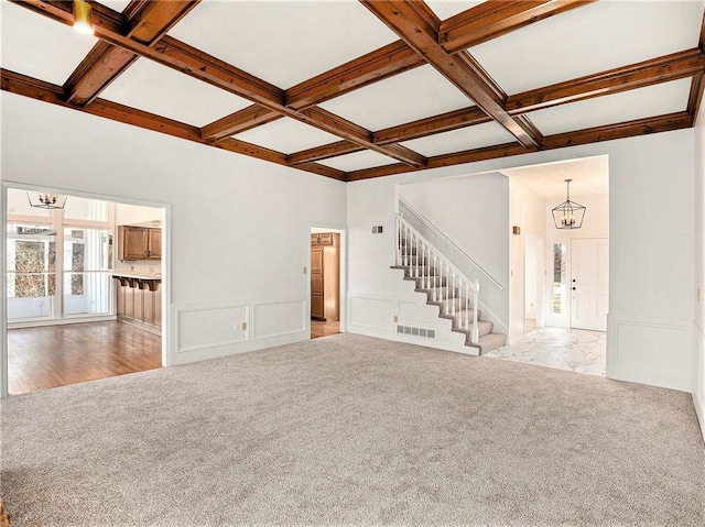 unfurnished living room featuring coffered ceiling, carpet, and an inviting chandelier