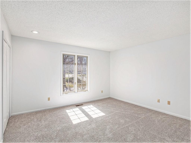 empty room with a textured ceiling, carpet, visible vents, and baseboards