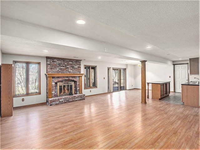 unfurnished living room featuring decorative columns, a fireplace, light wood finished floors, and a textured ceiling