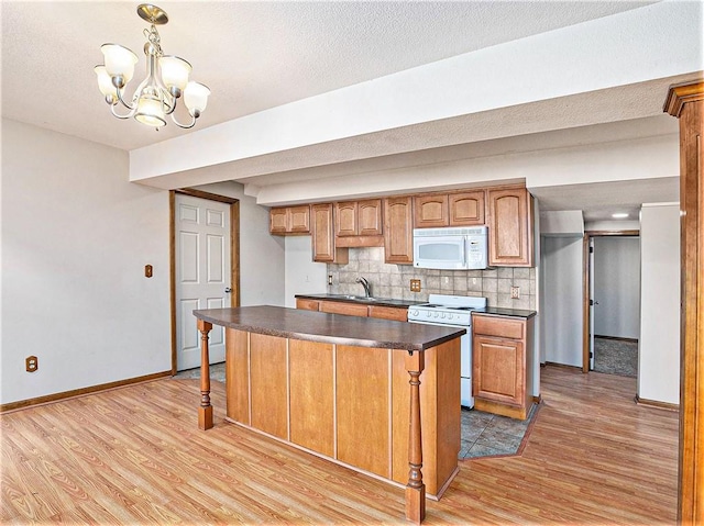 kitchen with a sink, backsplash, dark countertops, white appliances, and light wood-style floors