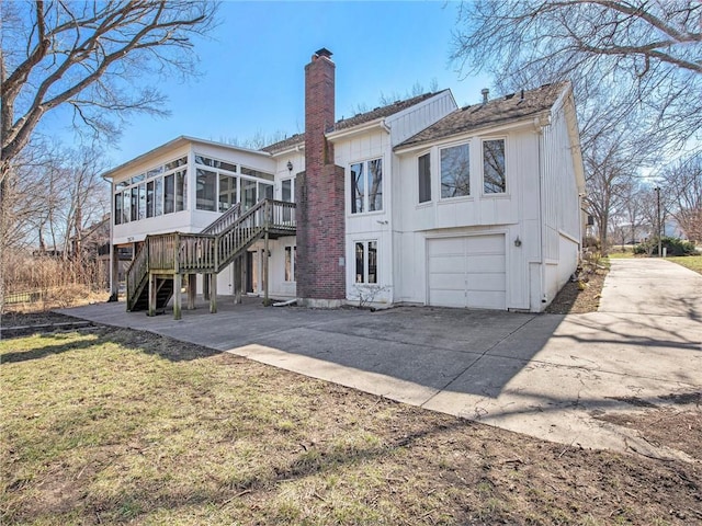 back of property featuring stairway, a sunroom, a chimney, concrete driveway, and a garage