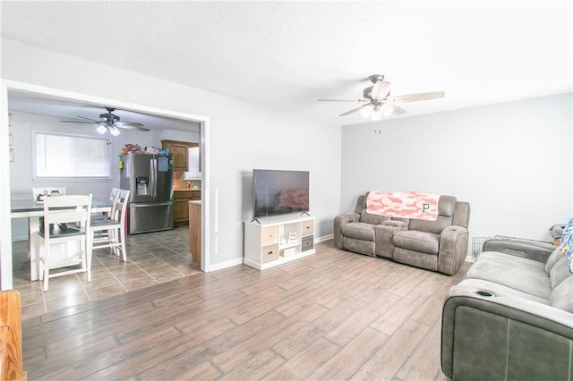 living area with a textured ceiling, wood finished floors, a ceiling fan, and baseboards