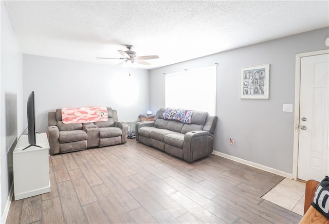 living room featuring a textured ceiling, ceiling fan, baseboards, and light wood-style floors