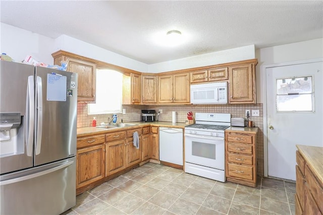 kitchen featuring light countertops, backsplash, a sink, a textured ceiling, and white appliances