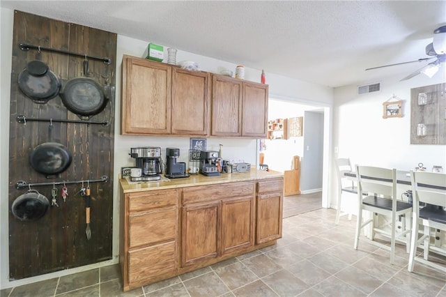 kitchen featuring light countertops, visible vents, a ceiling fan, brown cabinetry, and a textured ceiling