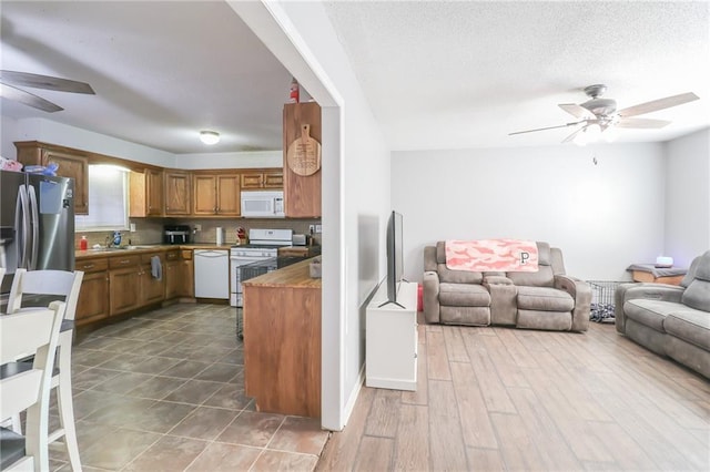 kitchen featuring white appliances, a sink, a ceiling fan, open floor plan, and brown cabinetry