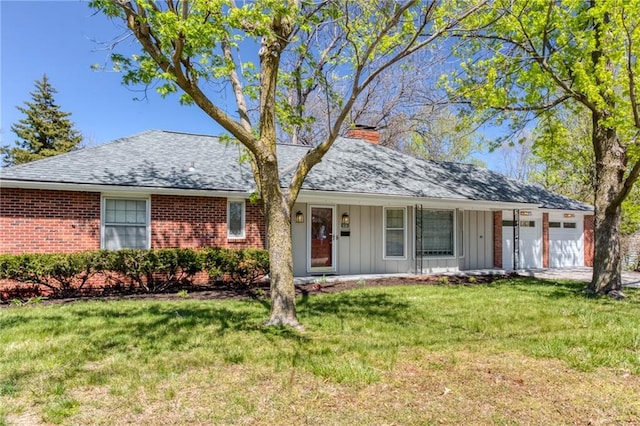 ranch-style home with board and batten siding, an attached garage, a front yard, brick siding, and a chimney