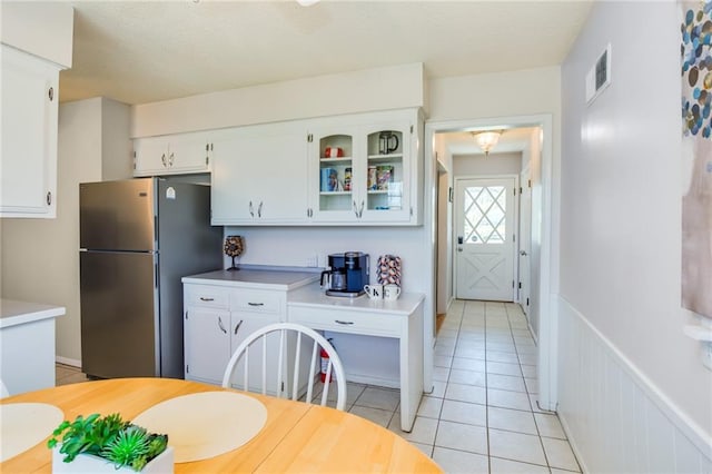 kitchen featuring freestanding refrigerator, light tile patterned flooring, white cabinets, light countertops, and glass insert cabinets