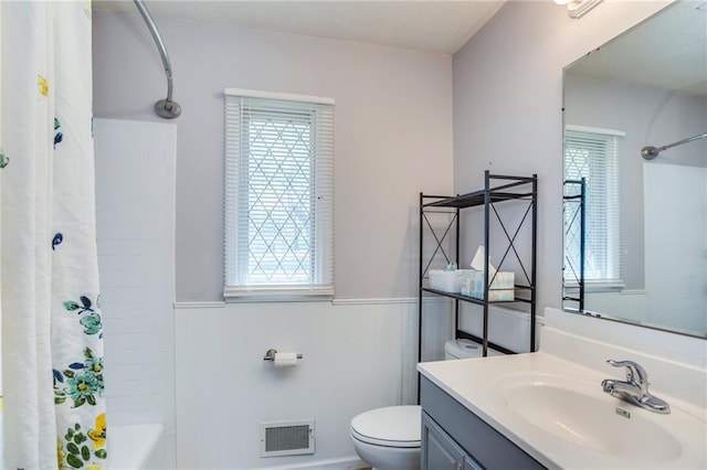 bathroom with visible vents, toilet, wainscoting, shower / tub combo, and vanity