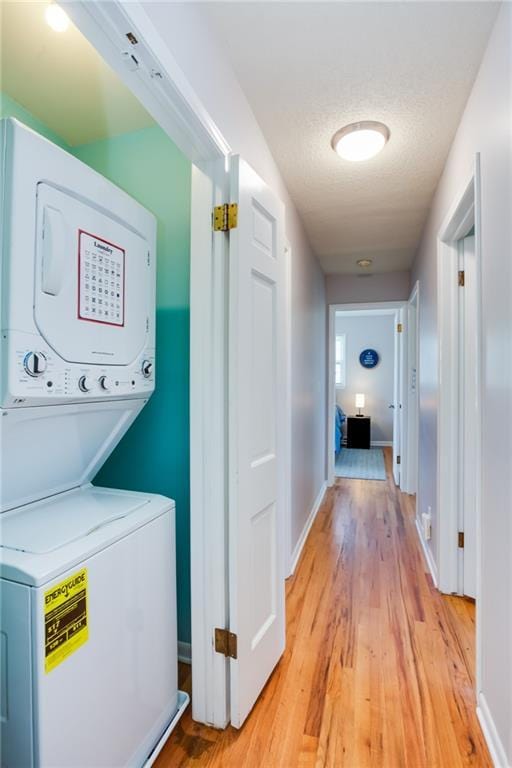 laundry area with baseboards, stacked washing maching and dryer, laundry area, light wood-style floors, and a textured ceiling