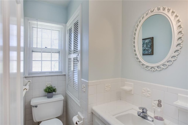 half bathroom featuring a sink, a wainscoted wall, toilet, and tile walls