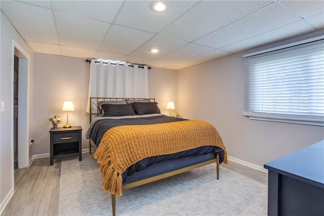 bedroom with a drop ceiling, baseboards, and light wood-style floors