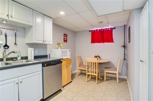 kitchen with white microwave, dark countertops, stainless steel dishwasher, white cabinets, and a sink