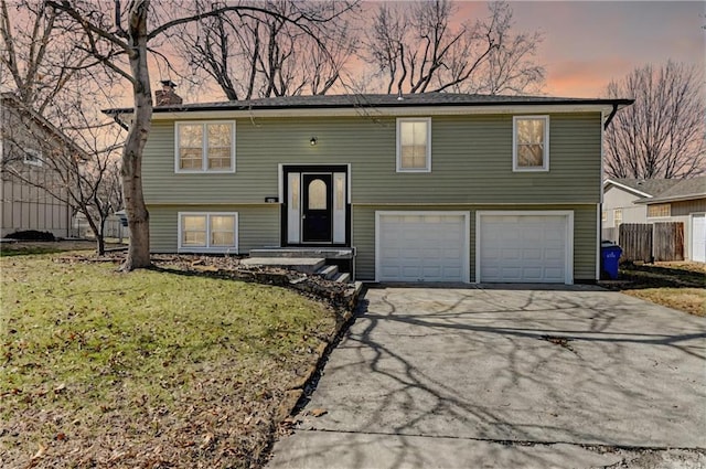 bi-level home with driveway, a front lawn, a garage, and fence