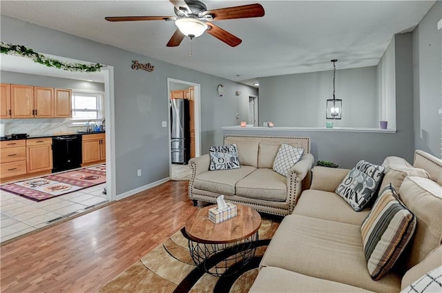 living room with light wood finished floors, ceiling fan with notable chandelier, and baseboards