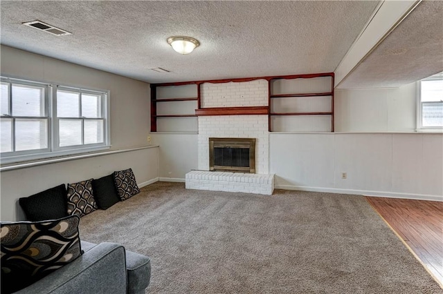 unfurnished living room with baseboards, visible vents, a textured ceiling, a brick fireplace, and carpet flooring