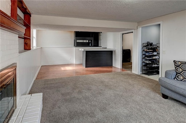 unfurnished living room with carpet floors, a textured ceiling, wood finished floors, and a fireplace