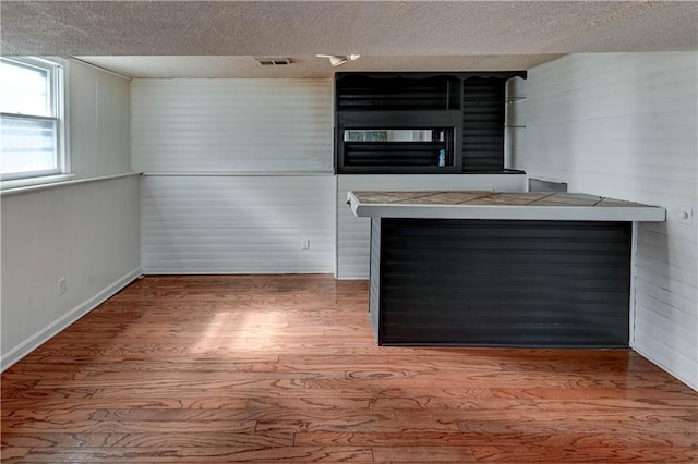 unfurnished living room featuring visible vents, a textured ceiling, wood finished floors, and a bar