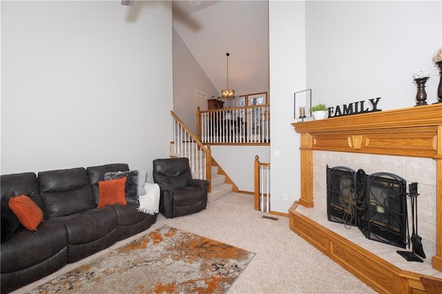 carpeted living room with stairway, visible vents, baseboards, high vaulted ceiling, and a tile fireplace