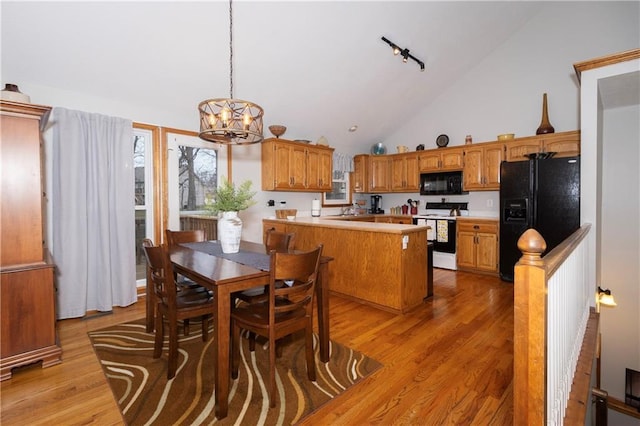 dining area with high vaulted ceiling, an inviting chandelier, light wood-style flooring, and rail lighting