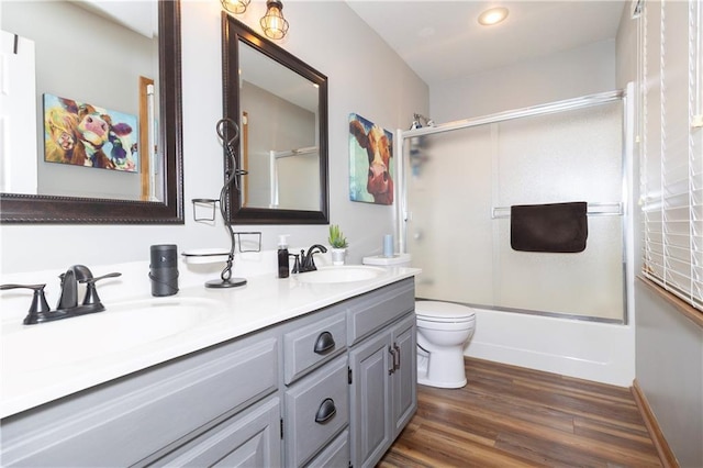 full bath with wood finished floors, double vanity, a sink, toilet, and combined bath / shower with glass door