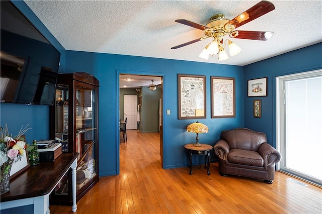 living area featuring wood-type flooring, ceiling fan, and a textured ceiling