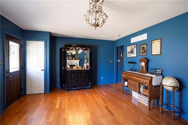 interior space featuring a textured ceiling, hardwood / wood-style floors, visible vents, and an inviting chandelier