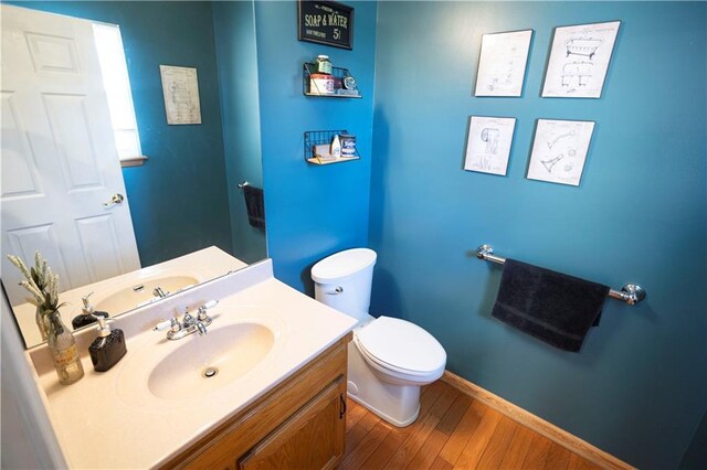 half bathroom with toilet, baseboards, wood finished floors, and vanity