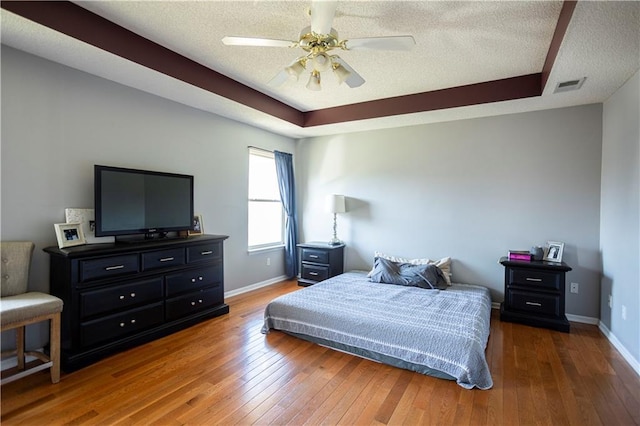 bedroom featuring hardwood / wood-style flooring, visible vents, and a tray ceiling