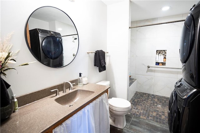 full bathroom featuring toilet, tiled shower, vanity, and stacked washer and clothes dryer