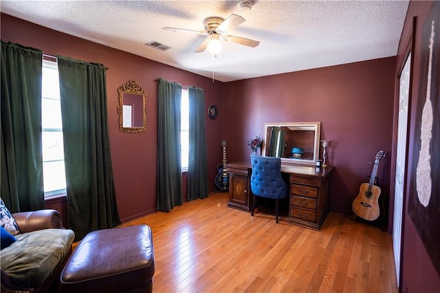 office space featuring light wood finished floors, ceiling fan, visible vents, and a textured ceiling