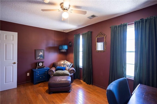 living area featuring a textured ceiling, ceiling fan, visible vents, baseboards, and hardwood / wood-style floors