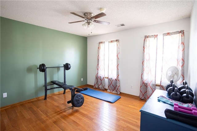 workout area with baseboards, visible vents, wood-type flooring, ceiling fan, and a textured ceiling