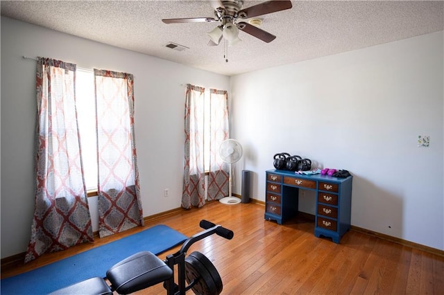 exercise area featuring visible vents, hardwood / wood-style floors, ceiling fan, a textured ceiling, and baseboards