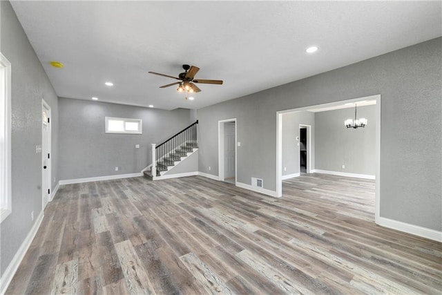 empty room featuring visible vents, baseboards, stairway, ceiling fan with notable chandelier, and wood finished floors