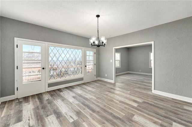 unfurnished dining area with a chandelier, wood finished floors, baseboards, and a textured wall