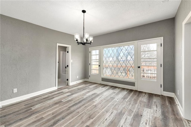 unfurnished dining area with a textured wall, baseboards, an inviting chandelier, and wood finished floors