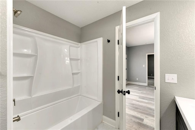 full bath featuring baseboards, a textured wall, shower / bathtub combination, wood finished floors, and vanity