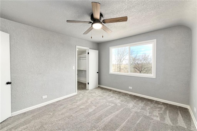 unfurnished bedroom featuring a walk in closet, a textured ceiling, carpet flooring, baseboards, and a textured wall