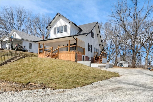 view of front of property with a deck, driveway, a front yard, brick siding, and stairs