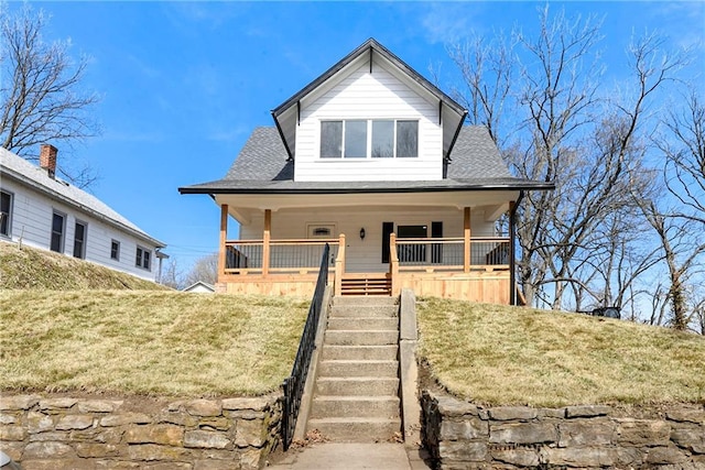 view of front facade with stairway, roof with shingles, a front yard, and a porch